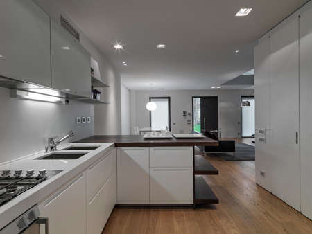 interior view of a modern living room in foreground the  kitchen whose floor is made of woodの写真素材