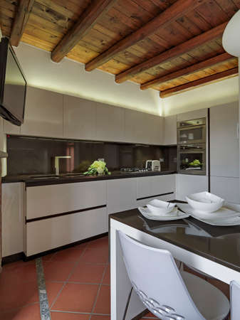 dishes in the foreground on the dining table in the modern kitchen whose floor is made of terracotta tiles and the ceiling is made of woodの写真素材