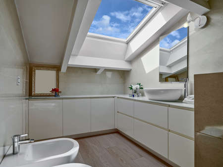 interiors of a modern bathroom in the attic room with skylight and wooden floorの写真素材