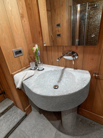 warm atmosphere in the rustic bathroom in the foreground the stone sink the walls are covered with wood panels the floor is made of stoneの写真素材