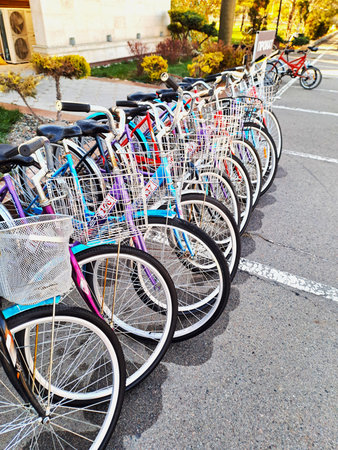 A collection of brightly colored bicycles with baskets is neatly parked in a row on asphalt, available for rent near a sign in a sunny outdoor areaの写真素材