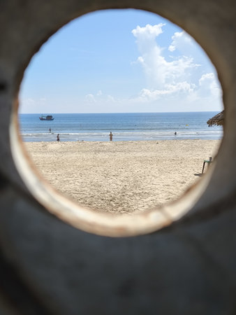 A captivating circular glimpse of the ocean, sandy shore, and blue sky with a boat in the distance, suggesting a perfect holiday sceneの写真素材