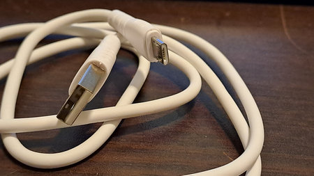 White USB cable on a wooden table. Close-up photo.