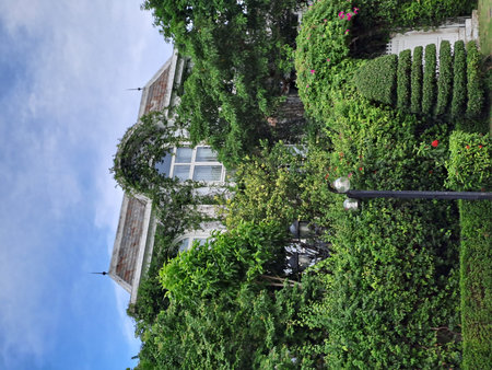 Elegant villa exterior hidden behind dense climbing plants and tropical garden vegetation. Decorative landscape architecture featuring topiary bushes and vintage street lamps underの写真素材