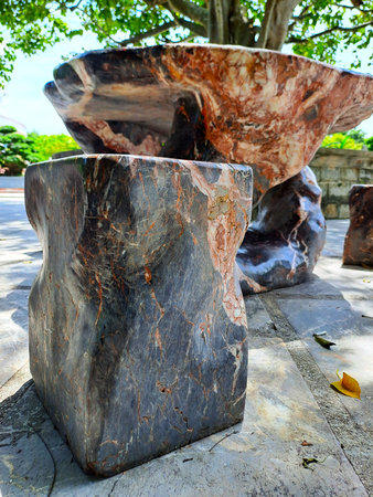 Heavy natural stone furniture with unique mineral patterns stands on a paved patio under the shade of treesの写真素材