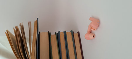 A stack of books and a pink earphone on a white background.