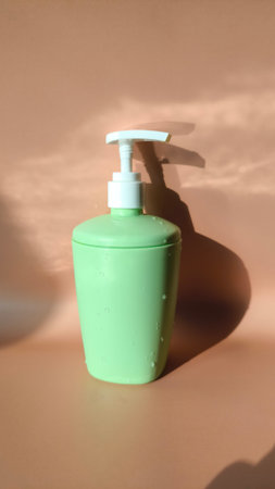 Green plastic soap dispenser with water droplets on a brown backgroundの写真素材