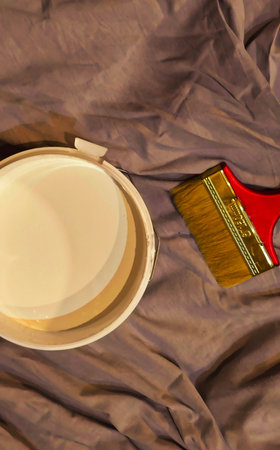 White paint bucket and brush on a brown background. Top view.