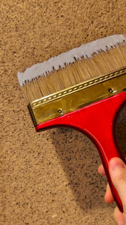 Person painting a textured wall with white paint using a wide brush