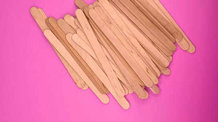 Wooden ice cream sticks on a pink background, top view.