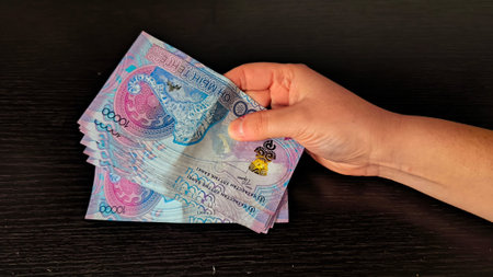 Female hand counting ten thousand tenge banknotes against a dark background. Concept of cash...