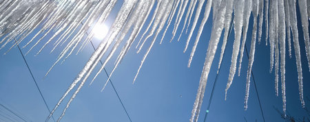 Shiny long icicles hanging against blue sky and bright sun.の写真素材