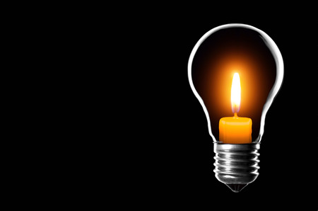 Lamp bulb inside a candle on a black background, with space for text.の写真素材