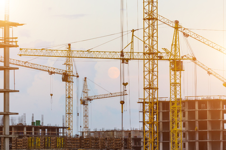 Industrial construction cranes and building silhouettes over sun at sunriseの写真素材