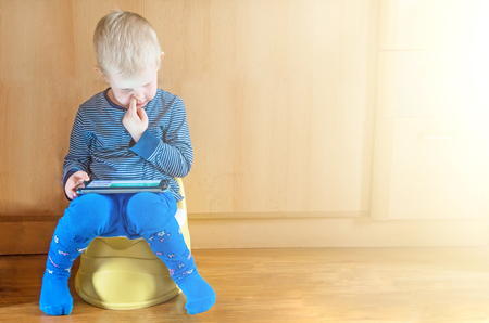 little boy on potty with tablet pc on the white carpetの写真素材