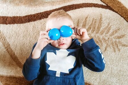 Boy lies on the floor and shows funny eyes with toysの写真素材
