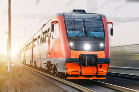 High-speed red passenger train rushing through the railway in the evening at sunset