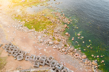 The shoreline from above, and the stones on it, building blocks, green algae in the waterの写真素材