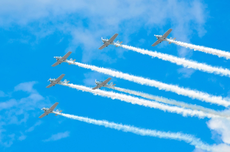 Group of white turboprop aircraft with a trace of white smoke against a blue sky