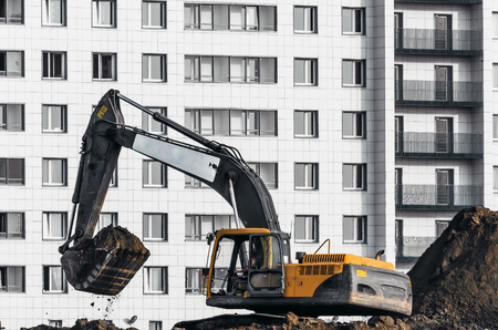 Excavator work on the ground on background of multi storey housesの写真素材
