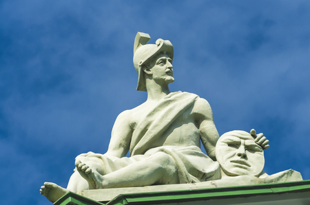 Ancient warrior sculpture sits and in the hands holds a circle disk with a face, a smileyの写真素材