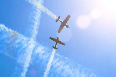 Two light engine aircraft with a trace of white smoke fly in the blue skyの写真素材