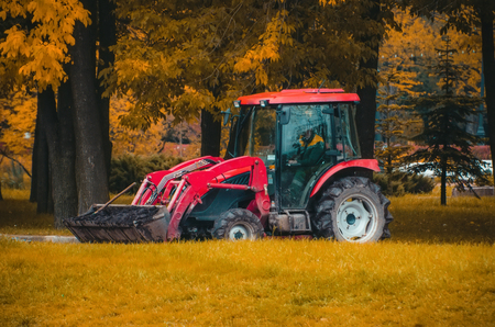Small red tractor in the autumn park transport the pots with flowers for planting