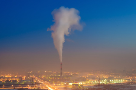 Single pipe with smoke in the industrial area of the city at nightの写真素材