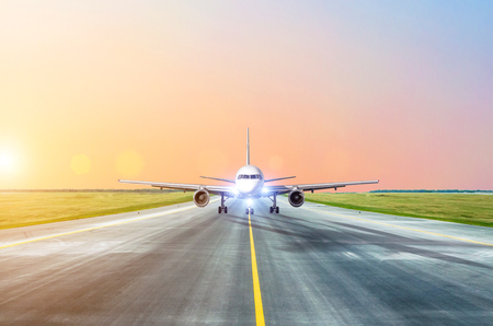 Aircraft taxiing on the runway at the airport at dusk with lights on, view of the nose of the cockpitの写真素材
