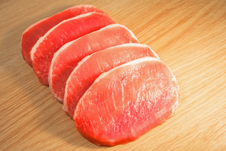 Five pieces of pork meat chopped on a board with a wooden textureの写真素材
