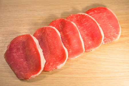 Five pieces of pork meat in a row chopped on a board with a wooden textureの写真素材