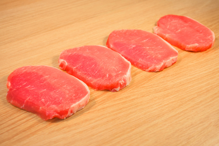 Four pieces of pork meat sliced on a wooden board with a boardの写真素材