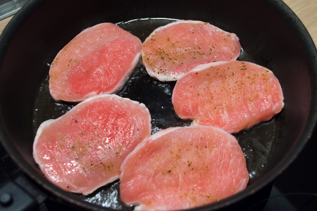 Five pieces of pork meat sprinkled with pepper, fry in a frying pan on one sideの写真素材