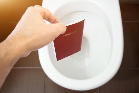 The hand holds the citizen's passport over the toilet, throw out his passport. The concept of change of citizenship, loss of passport, political problems, infringement of rightsの写真素材