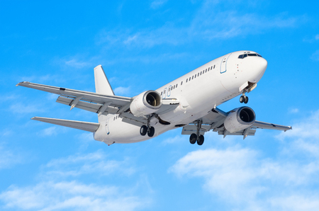 Passenger airplane with the chassis released before the landing at the airport against the blue sky