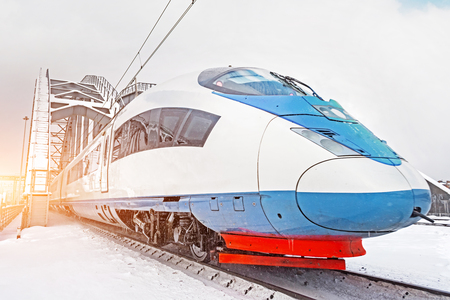 High-speed train rides at high speed metal railway bridge in winter around the snowy landscapeの写真素材