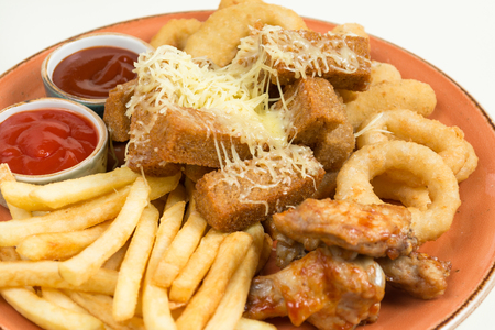 French fries, onion rings, chicken wings, rusks, a snack to beer on a large plate with two sauces on a brown backgroundの写真素材