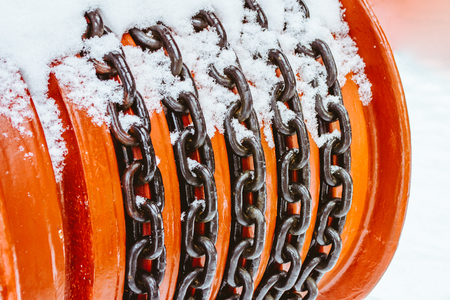 Metal black chain wound on a red drum and covered with snow in winterの写真素材