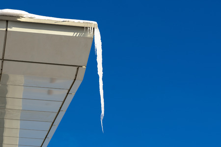 Huge single icicle of ice water on the edge of the roof in winter in the spring against a blue skyの写真素材