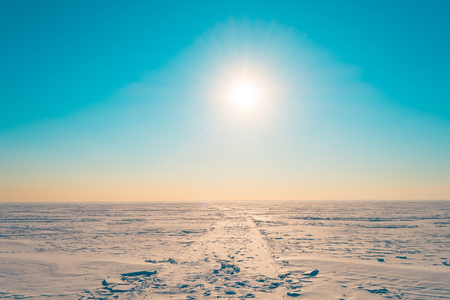 Road in the snow in the winter snowy desert in the turquoise sky the bright sun shinesの写真素材