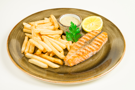 French fries and a piece of red fried fish salmon with a parsley leaf with sauce on a large plateの写真素材