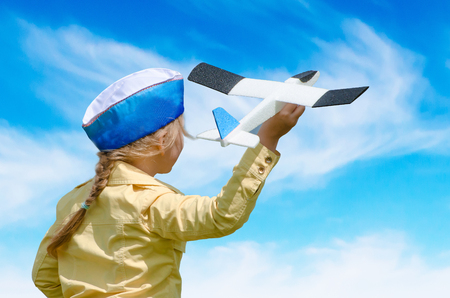 Happy baby girl kid playing with toy airplane against blue summer sky background. Concept - inoculating the love of children for aviationの写真素材