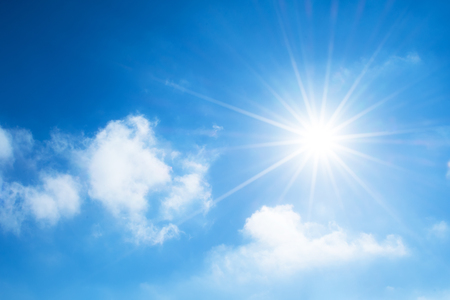 The sun with bright rays in the blue sky with white light cloudsの写真素材