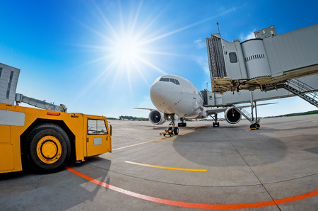 Parking at the airport, airplane at the teletrap. Aerodrome tractor is ready for towing and departure of the aircraft. Against the background of a blue sky and bright sun, nice weatherの写真素材