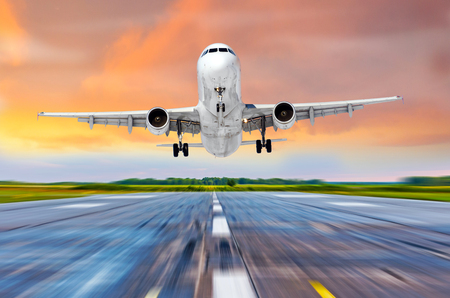Airplane flying arrival landing on a runway airport in the evening during a bright red sunset cloudscapeの写真素材