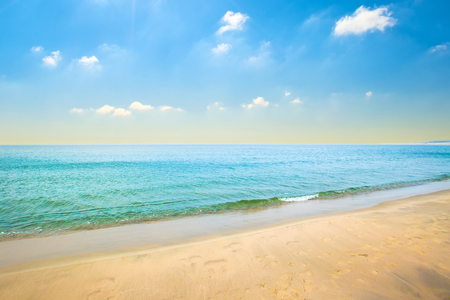 Sea sandy coast with blue water and small waves, clouds on a blue sky on a summer dayの写真素材