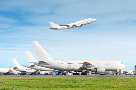 Passenger aircraft row, airplane parked on service before departure at the airport, other plane push back tow. One two-story airplane take off from the runway in the blue skyの写真素材