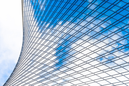 Reflection of sky and clouds in glass spiral, wave with bend facade windows of financial skyscrapers