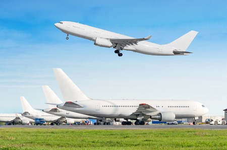 Passenger aircraft row, airplane parked on service before departure at the airport, other plane push back tow. One two-story airplane take off from the runway in the blue skyの写真素材