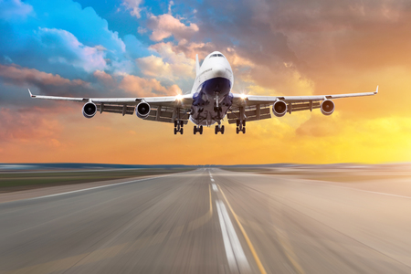 Airplane with four engines flying arrival landing on a runway in the evening during a bright red sunsetの写真素材